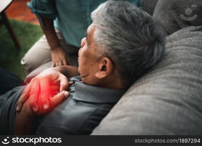Asian old elderly man is In pain with his hands on his chest and having a heart attack in the Living room and his wife is shocked and confused, helpless. Concept of healthcare and Elderly caregivers