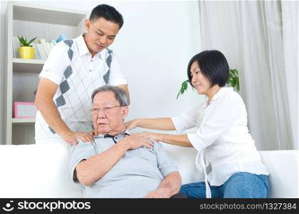 Asian old man shoulder pain, sitting on sofa , daughter and son massaging their father shoulder. Chinese family, senior retiree indoors living lifestyle at home.