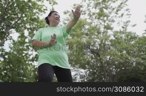 Asian overweight baby boom aged woman doing Chinese martial arts tai chi at the park, senior old age exercise healthy life, slow movement, relax calm meditation, mind body and nature synchronize
