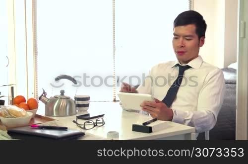 Asian people working at home with ipad, young business man at work with digital tablet computer and having breakfast in living room, portrait of happy businessman, busy male manager relaxing