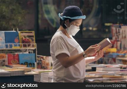 Asian plus size woman in protective face mask choosing book at book store in shopping mall area