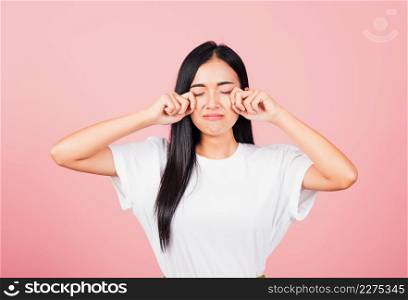 Asian portrait beautiful cute young woman bad mood her cry wipe tears with fingers, studio shot isolated on pink background, Thai female feeling sad unhappy crying with copy space