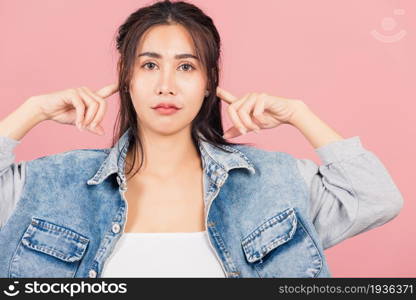 Asian portrait beautiful cute young woman wear denim plugging ears with fingers doesn&rsquo;t want to listen, studio shot isolated on pink background, Thai female covers ears for loud noise with copy space