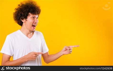 Asian Portrait happy young man curly hair White t-shirt pointing fingers away copy space isolated yellow background