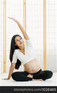 Asian Pregnant doing exercises with yoga by sitting and Meditating in japanese style house on the whit carpet, pregnant exercise concept, preparing to be motherhood with good healthy