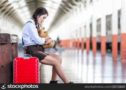 Asian pregnant woman traveler sitting on hugging Teddy Bear with a red suitcase at railway station travel,traveler with backpack in summer Holiday concept Thailand
