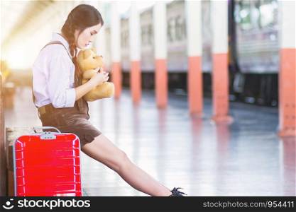 Asian pregnant woman traveler sitting on hugging Teddy Bear with a red suitcase at railway station travel, Belly girl