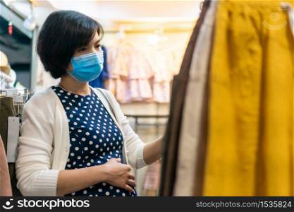 Asian Pregnant woman wear face mask shopping in a boutique, Young female looking and choosing baby clothing in a shop.