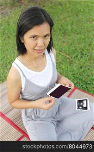 Asian Pregnant women show ultrasound film baby picture on her belly in hand at garden.