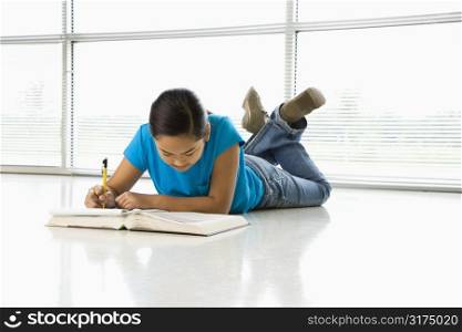 Asian preteen girl lying on floor doing homework.