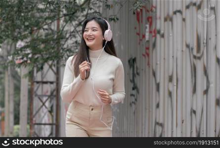 Asian pretty woman smiling, wearing headphone to listen music and running beside the street in the winter morning. Lifestyle Concept.