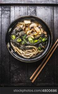 Asian ramen soup with noodles, tofu and nori seaweed in bowl with Chopsticks on dark wooden background.