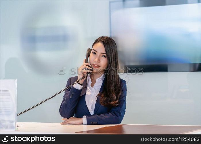 Asian reception recieving the call at the showroom counter for service the customer via telephone,