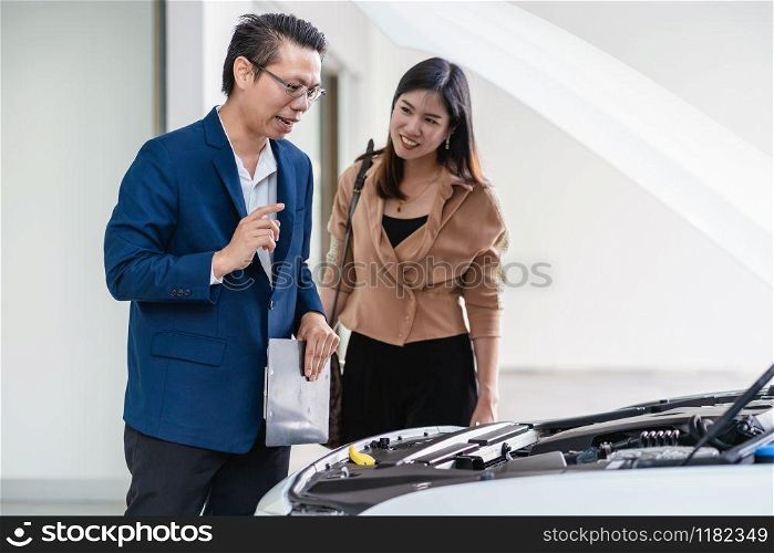 Asian receptionist open the car hood for checking and explaining the basic list of maintain to customer at maintainance service center for in showroom