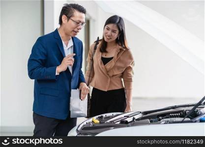 Asian receptionist open the car hood for checking and explaining the basic list of maintain to customer at maintainance service center for in showroom