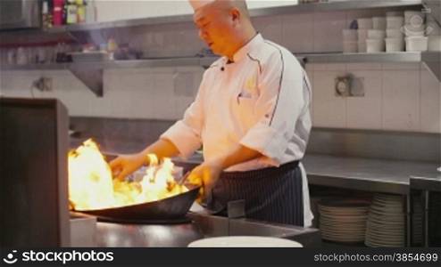 Asian restaurant, chinese chef cooking food, man as professional cook working, stir frying, preparing sauteed vegetables in pot on flame, fire, stove. Portrait, looking and smiling at camera. 24of27