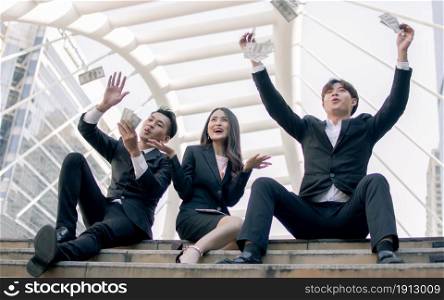 Asian rich business men and woman are very happy while sitting on stairs with a lot of money