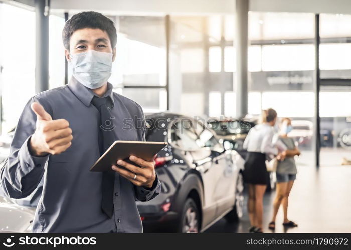Asian saleman wear surgical mask working in inspector checking writing on clipboard in garage of dealership Wait mechanic In showroom car and insurance new normol covid-19 in showroom dealership