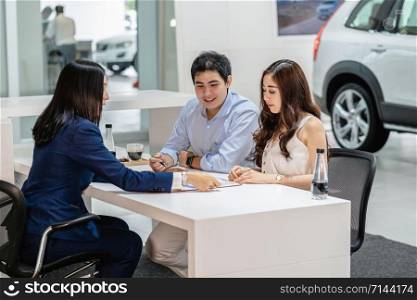 Asian Saleswoman explaining sales contract to couple customer before decision buy the new car in showroom