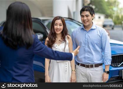 Asian Saleswoman welcoming the couple customer to checking the car infront of showroom, Customer service and sales representative concept