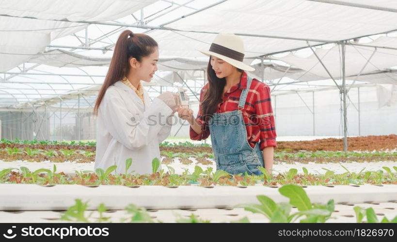 Asian scientist woman test solution chemical inspection soil in organic farm and show result to the owner in greenhouse, Woman farmer in a garden, Concept for new technology in the agriculture.