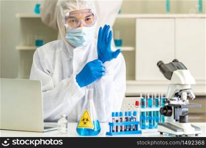 Asian Scientists with PPE suit put on medical glove in science laboratory before study research and experiment about coronavirus covid-19 vaccine. Medical Science technology and healthcare concept.