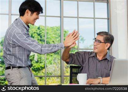 Asian senior and young business man greeting each other in the office. Happy old and junior two businessmen greet touch hand, greeting and partnership concept