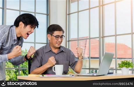 Asian senior and young business man people excited celebrating corporate victory together in office. Happy old and junior two businessmen video call conference on laptop computer success win triumph