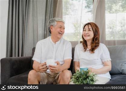 Asian senior couple relax at home. Asian Senior Chinese grandparents, husband and wife smile talking and drinking coffee while lying on sofa in living room at home concept.