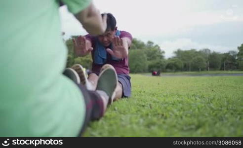 Asian senior couple stretching legs hand to toe sitting down on green grass public park, cool down after exercise family activities, retirement healthy life motivation, flexible body health condition