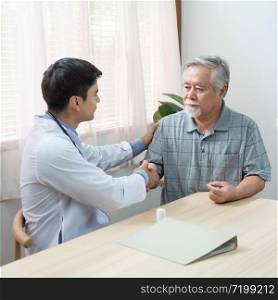 Asian senior elder man holding hand with greeting young caucasian doctor after know positive consulting and success examination at home.health care and medical concept.
