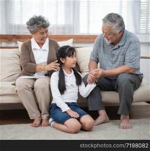 Asian senior Grandmother and happy asia elder grandfather sitting on sofa playing and enjoying leisure time with granddaughter in living in living at home or house, retirement old people concept.
