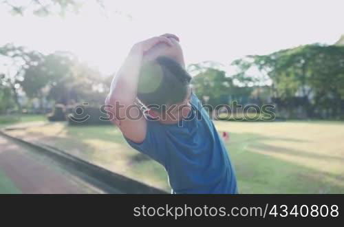 Asian senior man doing arms stretching warm up exercise inside the park, over head arm extension stretch, senior health care insurance, outdoor activities, vitality wellness fitness, sunny hot weather