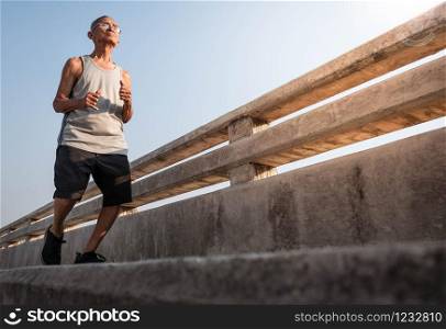 Asian senior man in sportswear jogging on bridge over sky background. Healthy lifestyle and Healthcare concept.