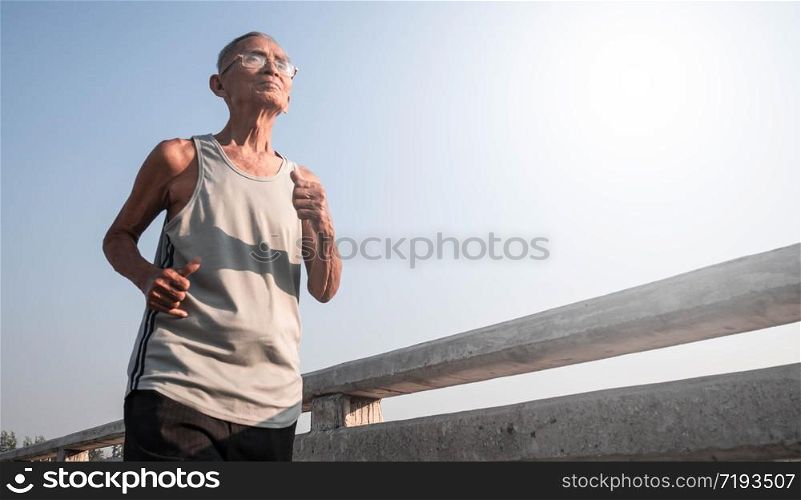 Asian senior man in sportswear jogging on bridge over sky background. Healthy lifestyle and Healthcare concept.