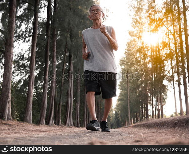 Asian senior man jogging in the park over sunset sky background. Healthy lifestyle and Healthcare concept.