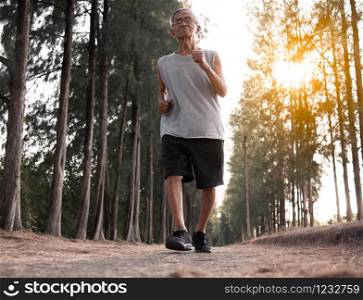 Asian senior man jogging in the park over sunset sky background. Healthy lifestyle and Healthcare concept.