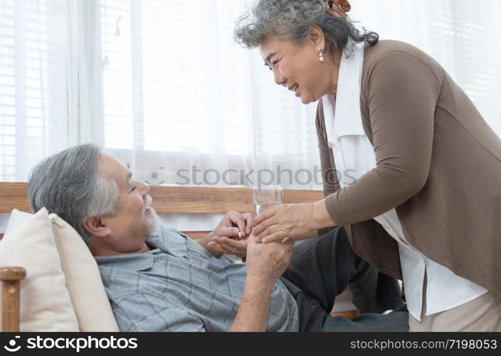 Asian Senior man taking medicines and drinking water while lie on couch. Old woman take care his husband while his illness at the house.