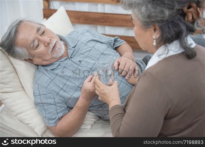 Asian Senior man taking medicines and drinking water while lie on couch at home, health and medicine concept with copy space.