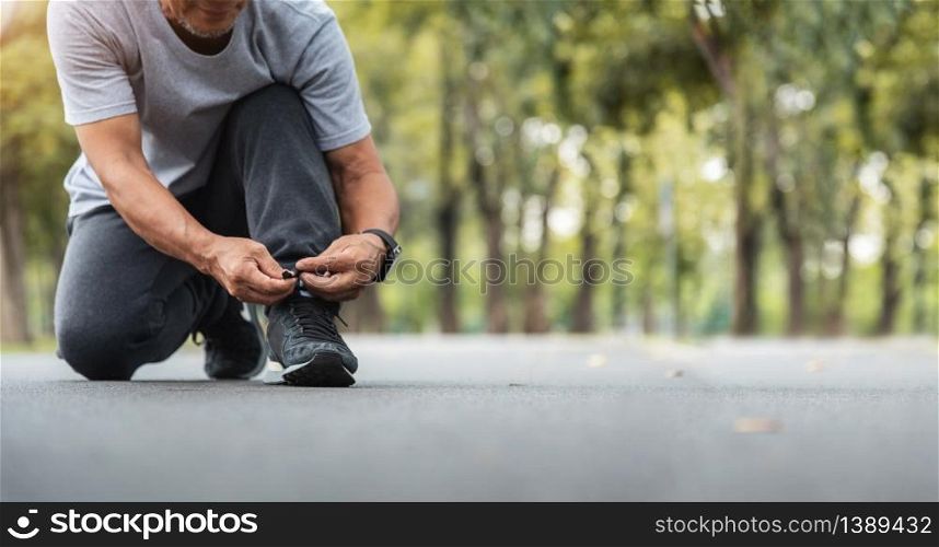 Asian Senior man tying running shoes at the park. Banner, Panoramic.