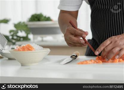 Asian senior man wear apron holding chopsticks to meticulous arrange sliced fresh salmon sashimi on bowl with ice. Japanese food home cooked concept