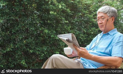 Asian senior men relax at home. Asian Senior Chinese male enjoy rest time wear glasses read newspaper and drink coffee while lying in the garden at home in the morning concept.