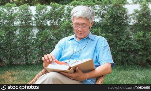 Asian senior men relax at home. Asian Senior Chinese male enjoy rest time wear glasses read books while lying in the garden at home in the morning concept.