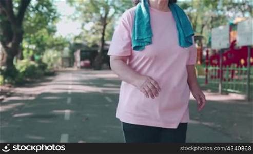 Asian senior obese female running inside the running track at the park on a sunny day in slow motion. Retirement lifestyle activity. Health care motivation, pulse blood pressure tracking, front view