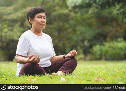 Asian Senior Woman in white shirt practicing Yoga at park. Thai Female in Meditation position with Copy space.