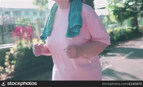 Asian senior woman jogging inside the park on a sunny day in slow motion. Retirement healthy life activity. over weight lady running, fight breast cancer, stay active and strong, hand held shot
