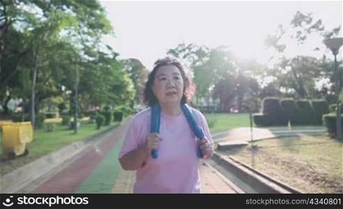 Asian senior woman jogging the park on a sunny day in slow motion. Retirement healthy life activity. Elderly Health care insurance plan, over weight lady running, fight breast cancer, tired struggle