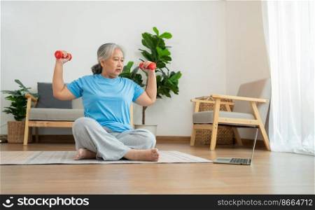 Asian senior woman lifting dumbbell for exercise and workout at home. Active mature woman doing stretching exercise in living room. Exercise Active and healthy for older, elder, and senior concept.