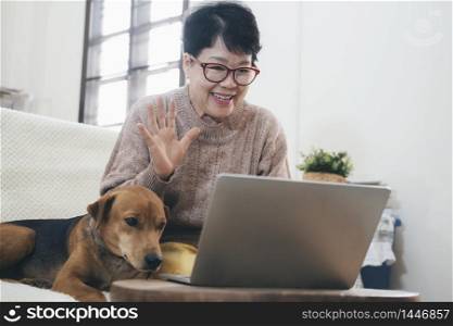 Asian senior woman making video call on laptop , waving at screen, chatting online with people who distance.