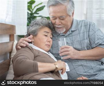 Asian Senior Woman taking medicines and drinking water while sitting on couch. Old man take care his wife while her illness at the house.